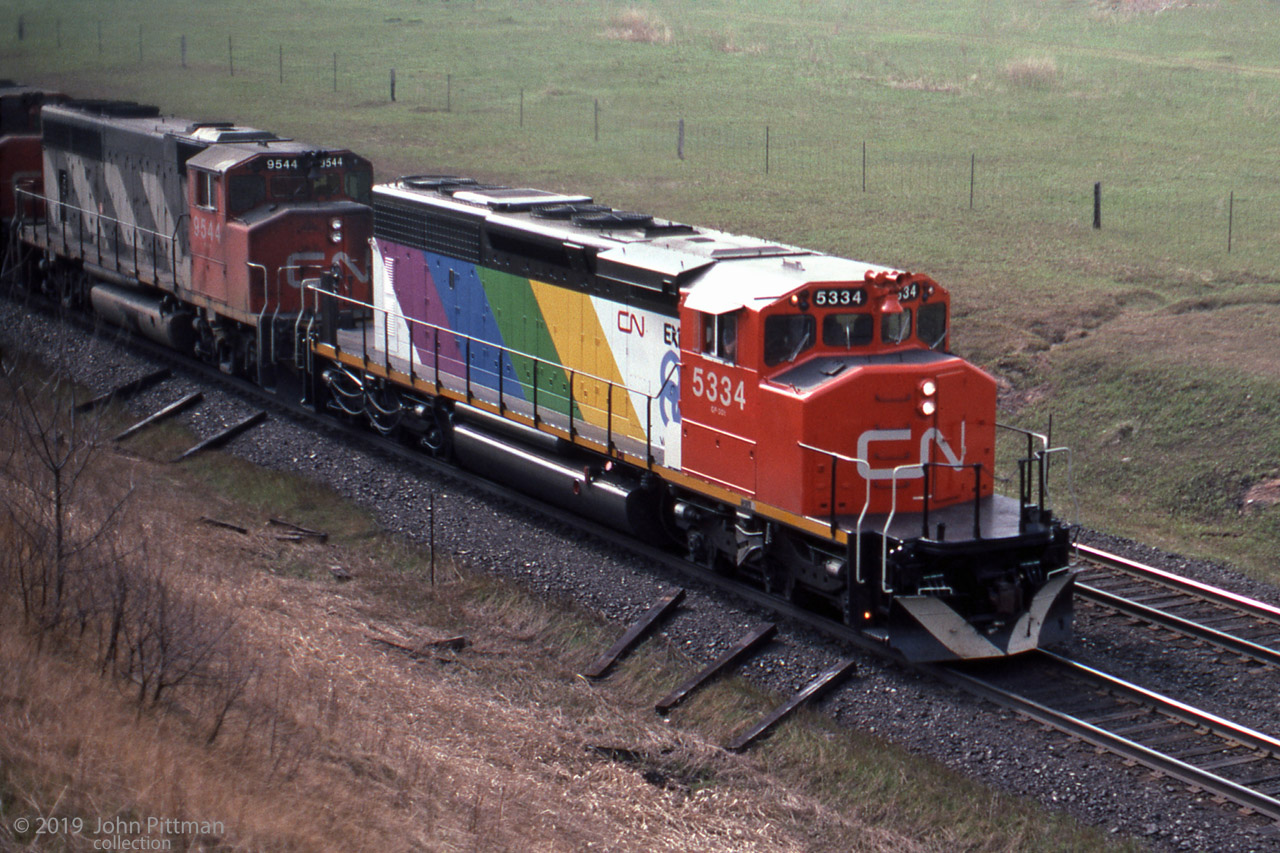 CN 5334, an SD40-2W built by GMD in 1980, was the only CN locomotive to receive an Expo 86 colour scheme.
This image taken from Newtonville Road bridge shows CN 5334 leading an eastbound train in the Spring of 1985. 
I believe the upper surfaces are gloss black, reflecting light from the sky.
CN also applied Expo 86 schemes to a few of their boxcars, the diagonal stripe colours varied.